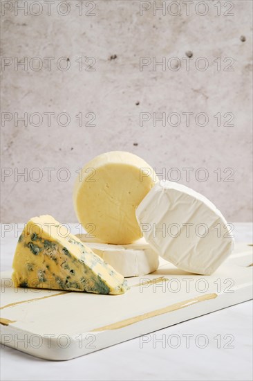 Pieces of brie, camembert, goat cheese and cheese with blue mold on wooden serving board
