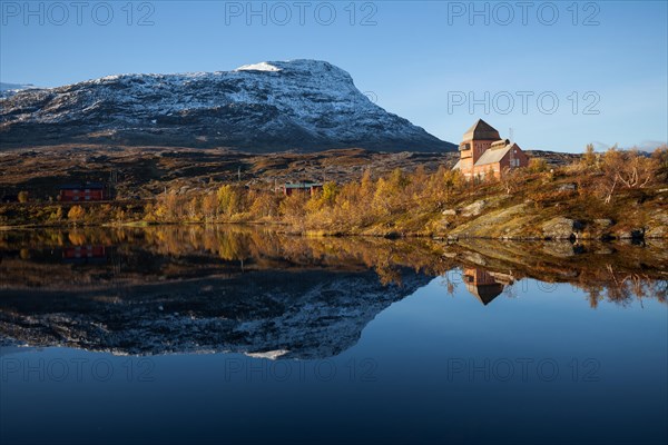 Northern Sweden, Vassijaure railway station with reflection in the lake. Snow-covered hilltop of the mountain Vassecohkka