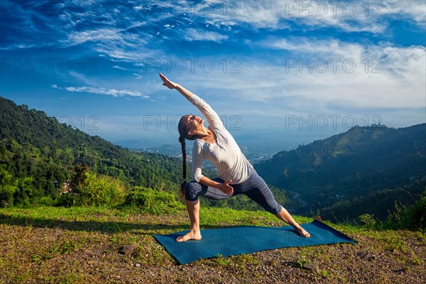 Woman practices yoga asana Utthita Parsvakonasana, extended side angle pose outdoors in mountains in the morning