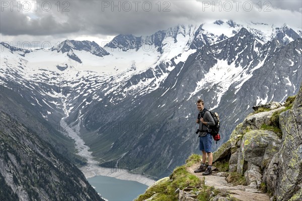 Mountaineer on hiking trail, view of Schlegeisspeicher, glaciated rocky mountain peaks Hoher Weisszint and Hochfeiler with glacier Schlegeiskees, Berliner Hoehenweg, Zillertal Alps, Tyrol, Austria, Europe
