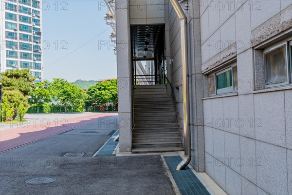 Rear entrance stairway into sports stadium with vacant paved lot, trees and blue sky in background