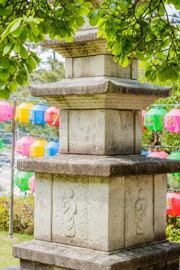 Stone carved pagoda under tree branches in front of colorful paper lanterns