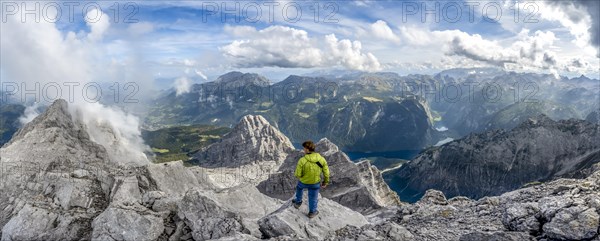 Mountaineer on the rocky summit of the Watzmann Mittelspitze, Watzmann crossing, view of mountain panorama with Steinernes Meer and Koenigssee, Berchtesgaden National Park, Berchtesgaden Alps, Bavaria, Germany, Europe