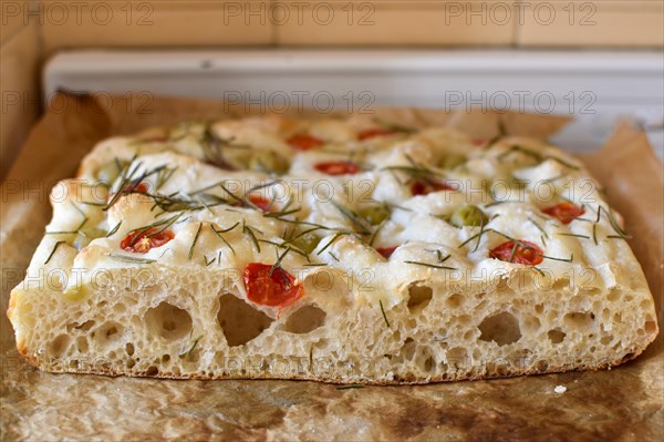 Homemade Italian flatbread focaccia with cherry tomatoes, olives and rosemary in a rustic kitchen