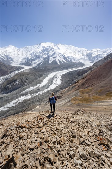 Mountaineer at Traveller's Pass with view of impressive mountain landscape, high mountain landscape with glacier moraines and glacier tongues, glaciated and snow-covered mountain peaks, Lenin Peak and Peak of the XIX Party Congress of the CPSU, Trans Alay Mountains, Pamir Mountains, Osh Province, Kyrgyzstan, Asia