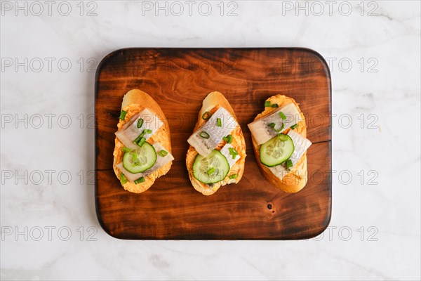 Top view of sandwiches with pieces of Clupeidae and spring onion on wooden serving board