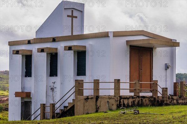 Side view of a small white country church sitting on a hillside in Guam with cloudy sky in the background