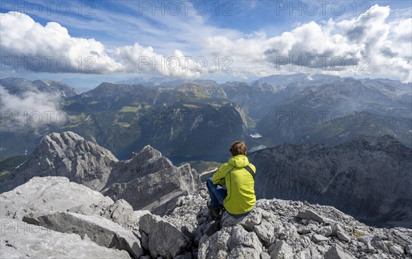 Mountaineer on the rocky summit of the Watzmann Mittelspitze, Watzmann crossing, view of mountain panorama with Steinernes Meer and Koenigssee, Berchtesgaden National Park, Berchtesgaden Alps, Bavaria, Germany, Europe