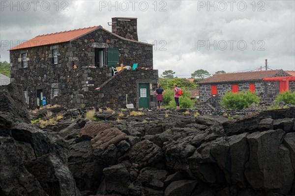 People standing next to a stone house on lava rock under an overcast sky, North Coast, Santa Luzia, Pico, Azores, Portugal, Europe