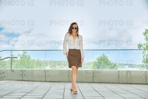 Stylish woman in mini crow's foot skirt and white blouse posing