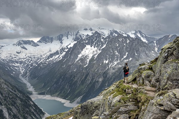 Mountaineer on hiking trail, view of Schlegeisspeicher, glaciated rocky mountain peaks Hoher Weisszint and Hochfeiler with glacier Schlegeiskees, Berliner Hoehenweg, Zillertal Alps, Tyrol, Austria, Europe