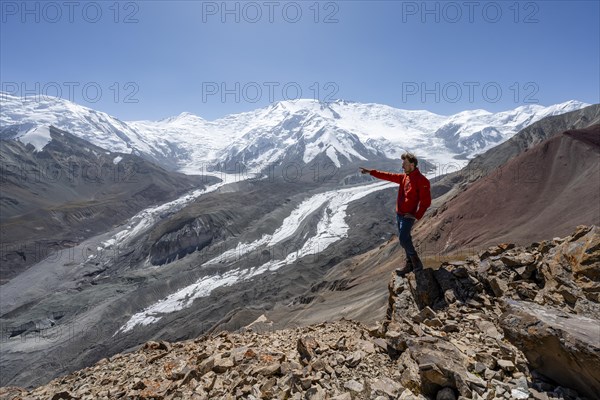 Mountaineer points into the distance, at Traveller's Pass with view of impressive mountain landscape, high mountain landscape with glacier moraines and glacier tongues, glaciated and snow-covered mountain peaks, Lenin Peak and Peak of the XIX Party Congress of the CPSU, Trans Alay Mountains, Pamir Mountains, Osh Province, Kyrgyzstan, Asia