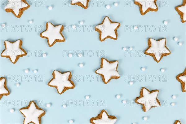 Top view of German star shaped glazed cinnamon Christmas cookies called 'Zimtsterne' on light blue background with snowball ornaments