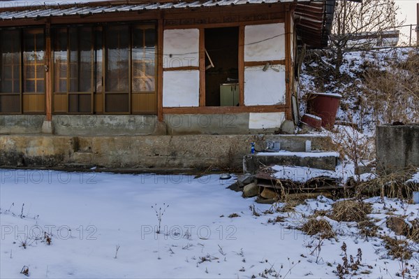 Old abandoned wooden house with sliding doors and concrete porch and snow covered lawn in a rural area in South Korea