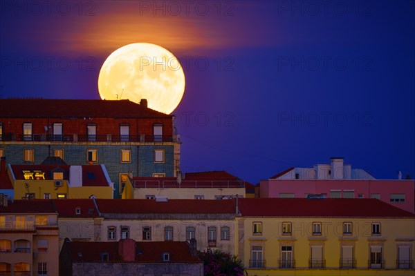 Beautiful view of big full moon rising behind a row of old houses in European city, Lisbon, Portugal. Supermoon, close up, Europe, night, landscape, cityscape, clear sky. Romantic evening, fairy tales, stories