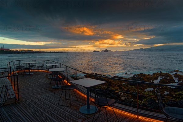 Terrace of the Cella Bar overlooking the coast of Madalena and the distant island of Faial at sunset under dramatic clouds, Madalena, Pico, Azores, Portugal, Europe
