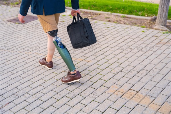 Rear view of an unrecognizable businessman with prosthesis walking along an urban park in summer