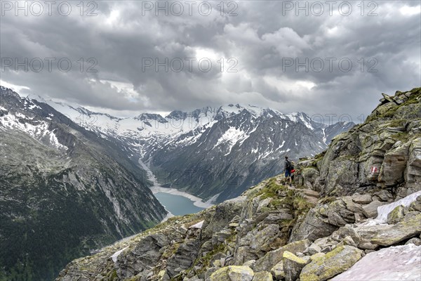 Mountaineer on hiking trail, view of Schlegeisspeicher, glaciated rocky mountain peaks Hoher Weisszint and Hochfeiler with glacier Schlegeiskees, Berliner Hoehenweg, Zillertal Alps, Tyrol, Austria, Europe