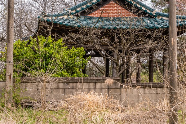 Old oriental style covered pavilion surrounded by a concrete wall in an overgrown woodland area in South Korea