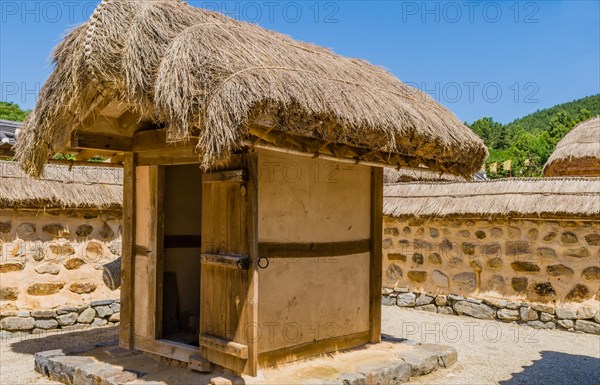 Buyeo, South Korea, July 7, 2018: Traditional outhouse with straw thatch roof and wooden door inside a mud and stone wall in public park at Neungsa Baekje Temple. For editorial use only, Asia