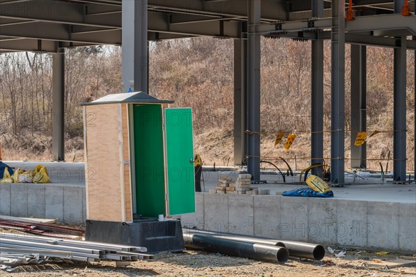 Chungju, South Korea, March 22, 2020: For editorial use only. Port-a-potty with open door at construction site next to unfinished industrial building, Asia