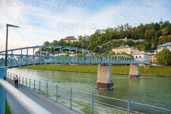 A long blue bridge over a river with green banks and blue sky, Mozartsteg, Salzburg, Austria, Europe