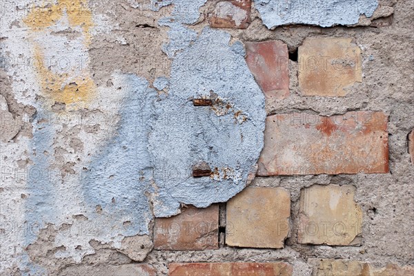A weathered wall with remains of plaster and exposed bricks, old wall of red bricks with blue, white and yellow colour on plaster remains, symbol of decay, vacancy, need for renovation, ageing, background, Mecklenburg-Vorpommern, Germany, Europe