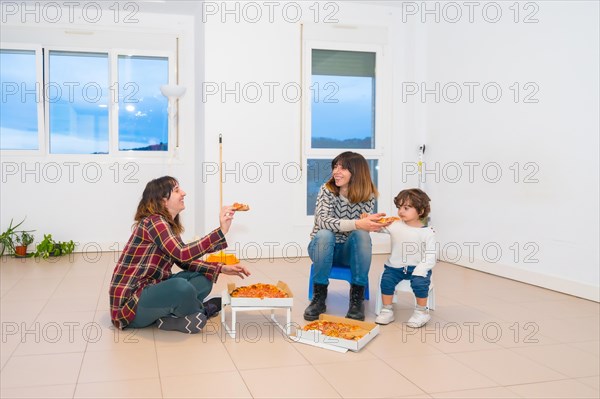 Lesbian couple and girl eating pizza in an empty house sitting on the floor without table