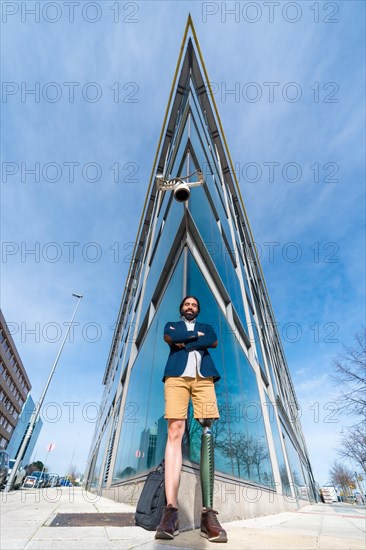Vertical portrait with low angle view of a businessman with prosthetic leg in the city outside office building