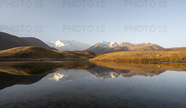 White glaciated and snowy mountain peak Pik Lenin at sunrise, mountains reflected in a lake between golden hills, Trans Alay Mountains, Pamir Mountains, Osh Province, Kyrgyzstan, Asia
