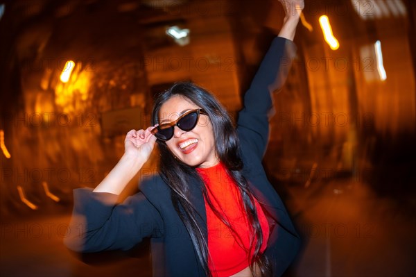 Night photo with flash and motion of a cool woman with sunglasses celebrating dancing in the city at night