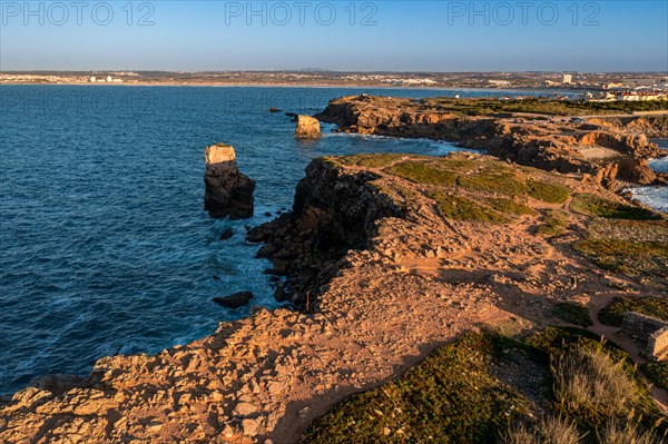 Bird's-eye view of ocean waves break on rocky shores pf Peniche, Portugal. Summer sunset haze, little foliage and rocky cliffs, peninsula and rocks, fishing town, horizon