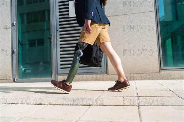 Lower part of an unrecognizable businessman with prosthetic leg walking along a financial district street