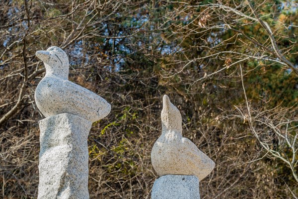 Closeup of stone carved ducks on vertical plinths in wilderness park with trees in fall colors