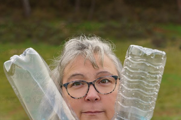 Close-up of an older white-haired woman with glasses holding two empty plastic bottles collected in the field, concept of ecology and care for the environment