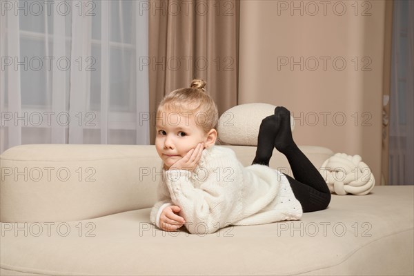Little girl lying on her stomach on sofa, looking at camera and propping her cheek