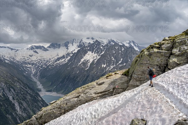 Mountaineer on hiking trail with snow, view of Schlegeisspeicher, glaciated rocky mountain peaks Hoher Weisszint and Hochfeiler with glacier Schlegeiskees, Berliner Hoehenweg, Zillertal Alps, Tyrol, Austria, Europe