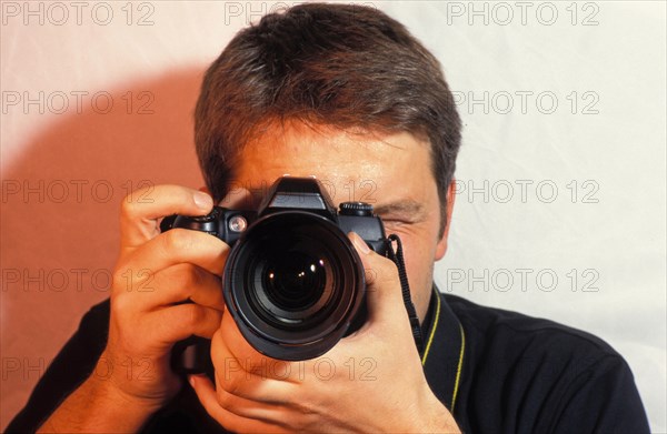 Young man, Photographer with camera taking a picture, focusing, portrait, camera in front of the face, looking through camera