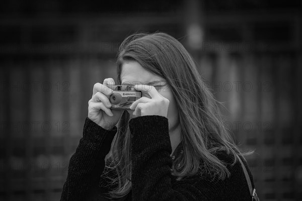 Young woman holds a camera in front of her face and concentrates on taking pictures, Hohenzollern Bridge, Cologne Deutz, North Rhine-Westphalia, Germany, Europe