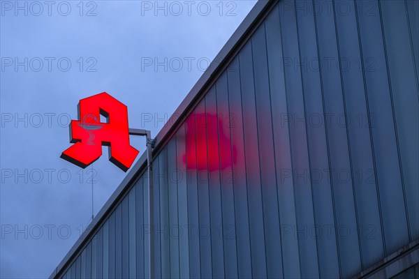 Illuminated pharmacy sign in front of a stormy sky on a facade in Duesseldorf, Germany, Europe