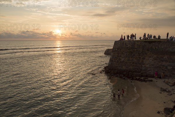 Tourists walk on fort ramparts at sunset in historic town of Galle, Sri Lanka, Asia