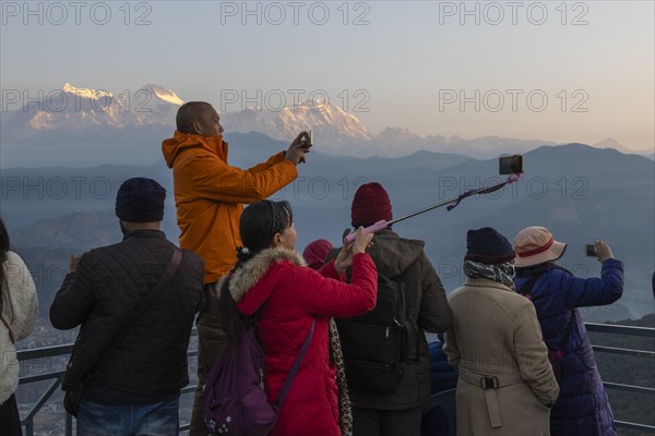 Asian-looking tourists watching and photographing sunrise as well as shooting selfies on the second day of the 2024 year from Sarangkot, with mountains of the Annapurna Massif in the background. Pokhara, Kaski District, Gandaki Province, Nepal, Asia