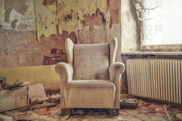 A worn armchair in front of a crumbling wall with falling wallpaper in an abandoned room, urologist's villa Dr Anna L., Lost Place, Bad Wildungen, Hesse, Germany, Europe