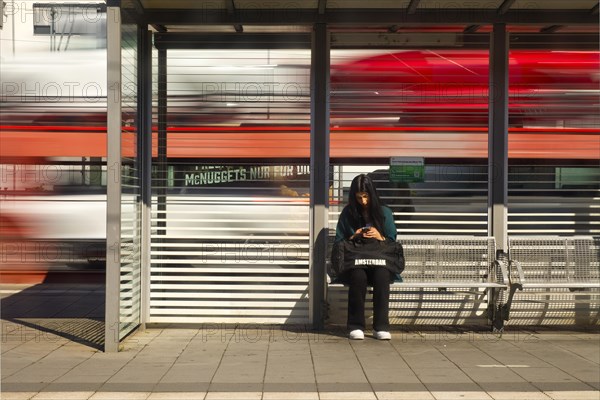 Young woman sitting on the platform looking at her mobile phone while a train passes by, Giessen Central Station, Hesse, Germany, Europe