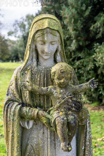 Green lichen growing on stone memorial statue of Mary and baby Jesus, Eddington, Hungerford, Berkshire, England, UK