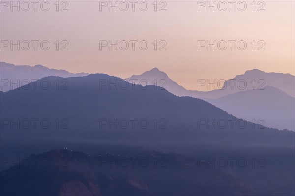Silhouette of the eight-thousander Manaslu and some other Himalayan peaks, including Ngadi Chuli, seen at daybreak from Sarangkot, the popular viewpoint above Pokhara, from the distance of nearly 70 km. The clear, January sky illuminates orange and violet, contrasting the contours of the dark mountains. Kaski District, Gandaki Province, Nepal, Asia