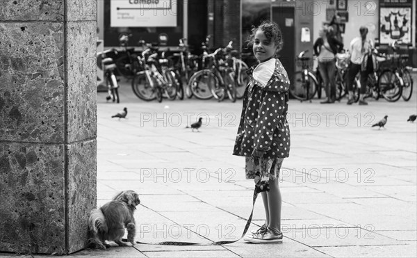 A little girl holds the leash of a dog on a city street, Hohenzollernbruecke, Cologne Deutz, North Rhine-Westphalia, Germany, Europe
