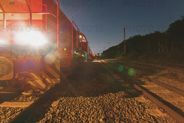 A red locomotive shines with its headlights on the tracks at night, Ruhr area, North Rhine-Westphalia, Germany, Europe