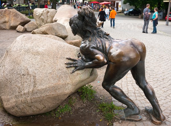 Bronze sculpture, statue, sculpture, sculpture, bronze witch grandmother Wadelinde, naked woman with sandals, slippers, slippers, spider on the backside and long fingernails, wild hairstyle, wild hair and rat on the shoulder pushes boulders, human backside, part of the figure group with devil and homununculus, witches dance place, boulders, tourists walking and standing on paths in the background, Thale, Eastern Harz, Harz, Saxony-Anhalt, Germany, Europe