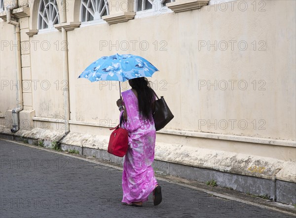 Woman walking with umbrella for shade by the fort walls in the historic town of Galle, Sri Lanka, Asia